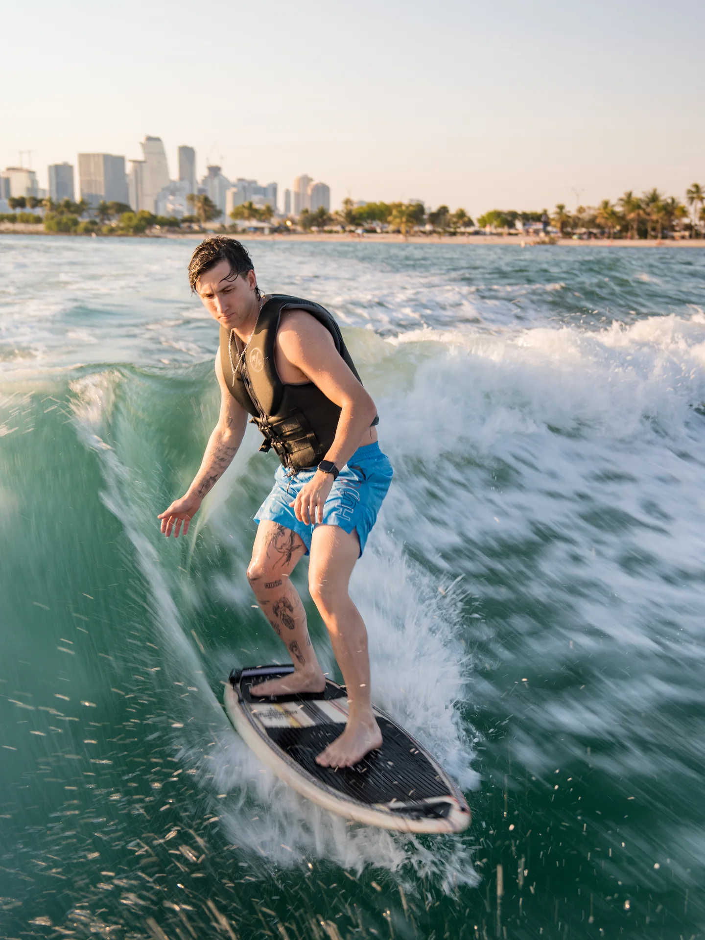 A wakesurfer riding a turquoise wave with the Miami skyline behind him